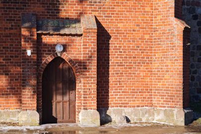 Fragment południowej ściany kościoła; na prawo do drzwi kamień z wyrytą głową