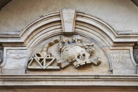 Detal epitafium Christopha Hacknera – przedstawienie czaszki ze skrzyżowanymi kośćmi oraz narzędzi geometrycznych odnoszących się do zawodu murarza i architekta; po bokach sentencje łacińskie o charakterze memento mori.